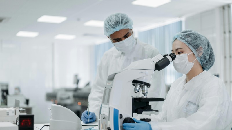 Scientists in protective suits examining samples under a microscope, focusing on microbiological research., tags: de dans la - pexel
